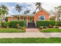 Charming peach home featuring a welcoming front porch, brick walkway, and lush tropical landscaping at 114 Mcgregor St, Punta Gorda, FL 33950