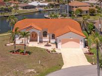 Waterfront home featuring an orange tile roof, lush landscaping, and a private driveway leading to an attached garage at 3705 Toulouse Ct, Punta Gorda, FL 33950