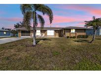 Charming single-story home with a well-maintained lawn, palm trees, and a cozy seating area on the porch at 3480 Pinetree St, Port Charlotte, FL 33952