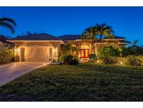 Beautiful home at dusk, featuring a lush lawn, tropical landscaping, and a vibrant red front door at 211 Lido Dr, Punta Gorda, FL 33950