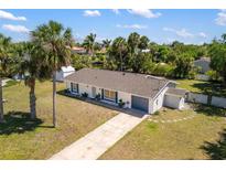 Single-story home with a well-manicured lawn, palm trees, and a long driveway in a sunny setting at 18263 Ohara Dr, Port Charlotte, FL 33948