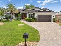 Inviting single-Gathering home with a well-manicured lawn, palm trees, brick driveway, and a two-car garage at 340 Belaire Ct, Punta Gorda, FL 33950