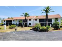 Condominium building featuring a red tile roof and white exterior with mature tropical landscaping and a paved parking lot at 2275 S Mccall Rd # 103, Englewood, FL 34224