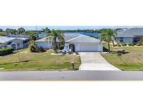 Inviting single-story home with a well-manicured lawn, palm trees, and a long driveway leading to an attached garage at 318 Spring Lake Nw Blvd, Port Charlotte, FL 33952
