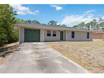 Charming single-story home featuring a green garage door and front door, set against a lush treed background at 105 Biscayne Dr, Port Charlotte, FL 33953