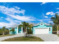 Charming, light blue single-story home with a well-manicured lawn, two-car garage, and tropical landscaping at 8084 Burwell Cir, Port Charlotte, FL 33981
