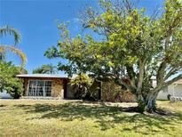 Charming single-story home featuring a stone facade, mature trees, and lush green lawn at 261 Caddy Rd, Rotonda West, FL 33947