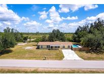 Ranch-style home with a pool, front porch, long driveway, and large yard under a cloudy blue sky at 30154 Beech Rd, Punta Gorda, FL 33982