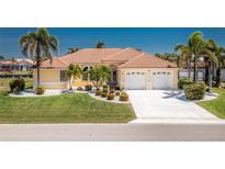 Charming yellow home featuring a tile roof, a well-manicured lawn, and a two-car garage, all under a bright blue sky at 910 Via Tripoli, Punta Gorda, FL 33950