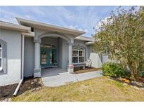 Charming home featuring a teal double-door entrance, pillars, and lush landscaping at 1513 Urmey Ln, North Port, FL 34286