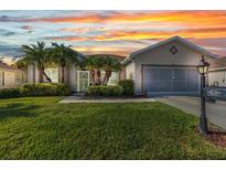 Charming single-story home featuring lush lawn, mature landscaping, and a two-car garage at sunset at 24371 Folkstone Ave, Punta Gorda, FL 33980