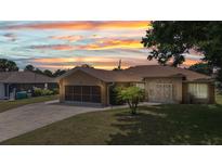 Charming single-story home with well-manicured lawn, attached garage, and security gate at entry under a colorful sunset sky at 78 Zenith St, Port Charlotte, FL 33954