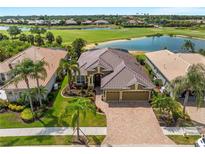 Stunning aerial view of a tile roofed home with a three car garage, lush landscaping, and water views at 5461 White Ibis Dr, North Port, FL 34287