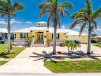 Inviting yellow home with white trim, double doors, and mature palm trees set against a clear blue sky at 233 Beeney Se Rd, Port Charlotte, FL 33952