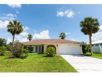Single-story home with a two-car garage, tropical landscaping, a green lawn, and a sunny blue sky at 1612 Blue Lake Cir, Punta Gorda, FL 33983