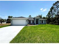 Charming single-story home with a well-manicured lawn and a two-car garage with blue sky at 7381 De Brita Rd, North Port, FL 34291