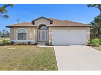 Inviting single-story home with a well-manicured lawn, arched windows, and a two-car garage at 118 Naomi Pl, Rotonda West, FL 33947