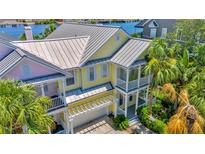 Inviting yellow two-story home with metal roof, dual balconies, lush tropical landscaping, and pergola-covered driveway at 936 Hemingway Cir, Tampa, FL 33602