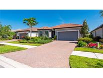 Charming single-story home with a red tile roof, brick driveway, lush landscaping, and a two-car garage at 1470 Hyssop Loop, North Port, FL 34289