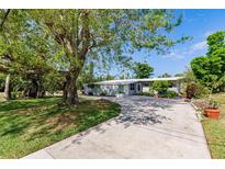 Charming single-story home featuring a lush front yard with mature trees, complemented by a long driveway on a sunny day at 3129 Buttonwood Pl, Punta Gorda, FL 33950