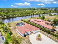 Expansive property features a red tile roof, waterfront access, circular driveway, and screened pool, surrounded by lush greenery at 13295 Eisenhower Dr, Port Charlotte, FL 33953