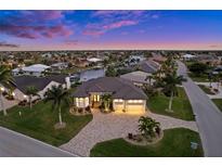 Waterfront home boasts lush landscaping, paver driveway and a three-car garage at dusk at 1932 Los Alamos Dr, Punta Gorda, FL 33950