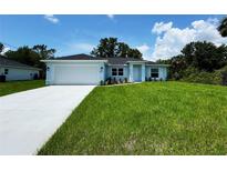 Charming light blue single-story home featuring a lush green lawn and a two-car garage at 8667 Lisa Blvd, North Port, FL 34288