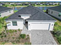 Aerial view of a well-maintained home with a gray roof, paver driveway, lake view, and manicured landscaping at 15069 Anchorage Rd, Punta Gorda, FL 33982