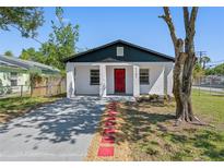 Charming single-story home with a red door, gray driveway, and fresh landscaping in a fenced yard at 2101 W Cherry St, Tampa, FL 33607