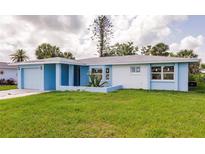 Charming single-story home showcasing a light blue and white exterior, green lawn, and attached garage at 37 Oakland Hills Ct, Rotonda West, FL 33947