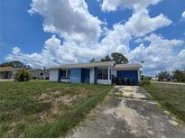 Single story house with blue and white exterior paint, overgrown lawn, and driveway with parked garbage bins at 4424 Baroda Ave, North Port, FL 34287
