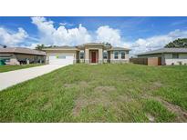 A single-Gathering home featuring a well-maintained lawn, neutral tones, and a red entry door at 1057 Presque Isle Dr, Port Charlotte, FL 33952