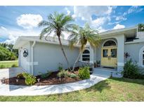 Charming home entrance with a yellow double door and palm trees in the front yard at 976 Great Falls Nw Ter, Port Charlotte, FL 33948