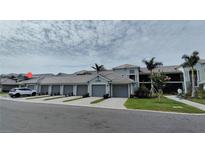Condominium exterior with private garages, tropical landscaping, and paver driveway under partly cloudy skies at 12390 Wellen Golf St # 202, Venice, FL 34293
