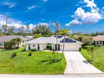 Inviting single-story home boasts a well-manicured lawn, solar panels, a two-car garage, and lush landscaping at 18147 Brazil Ave, Port Charlotte, FL 33948