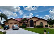 Inviting single-story home featuring a metal roof, arched windows, lush landscaping, and a spacious driveway at 214 Castile Ct, Punta Gorda, FL 33983