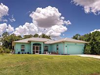 Charming single-story home with turquoise exterior, manicured lawn, and attached two car garage beneath a partly cloudy sky at 2969 Wells Ave, North Port, FL 34286