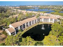 Scenic aerial view of the condo complex with a pond and fountain amidst lush greenery, showcasing waterfront living at 1144 Bird Bay Way # 102, Venice, FL 34285