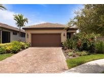 Charming single Gathering home featuring a tile roof, brick driveway, and lush landscaping at 13935 Campoleone St, Venice, FL 34293