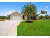 Tan one-story house with a two-car garage and lush lawn at 15889 Viscount Cir, Port Charlotte, FL 33981