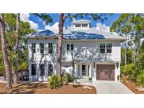 Two-story home with a metal roof, white siding, inviting entryway, and attached garage on a sunny day at 7064 Baypine Ln, Englewood, FL 34224