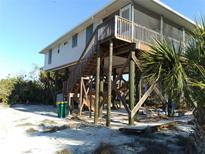 Coastal home on stilts featuring a wooden deck and staircase, surrounded by lush tropical foliage at 91 Gasparilla Way, Placida, FL 33946