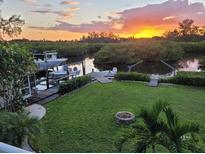 Waterfront property with grassy yard, dock, boat lift, and fire pit offering relaxing outdoor living, against a gorgeous sunset view at 900 Oxford Dr, Englewood, FL 34223