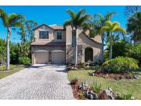 Inviting two-story home featuring a stone facade, paver driveway, and lush tropical landscaping at 117 Cable Dr, Rotonda West, FL 33947