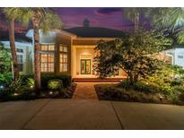 Beautifully landscaped home exterior with manicured bushes, palm trees, and a brick walkway at dusk at 790 N River Rd, Venice, FL 34293
