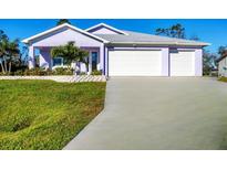 Charming one-story home featuring a three-car garage, manicured lawn, and a delightful, light purple exterior at 7499 Ashtabula St, Englewood, FL 34224
