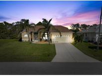 Charming single-story home with a well-manicured lawn and two-car garage, framed by mature palm trees at dusk at 127 White Marsh Ln, Rotonda West, FL 33947