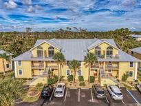 Yellow condo building with metal roof, balconies, and palm trees in front of ample parking at 6610 Gasparilla Pines Blvd # 111, Englewood, FL 34224
