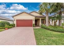 Charming single-story home featuring a red brick driveway, manicured lawn, and a red garage door at 2628 Sherman Oak Dr, North Port, FL 34289