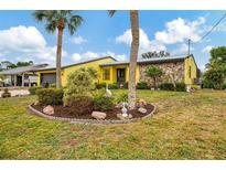 Charming yellow home featuring stone accents, a well-manicured lawn, and beautiful palm trees at 1173 Brown St, Englewood, FL 34224